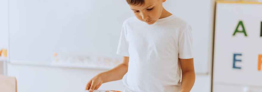 boy standing inside a classroom looking at a book